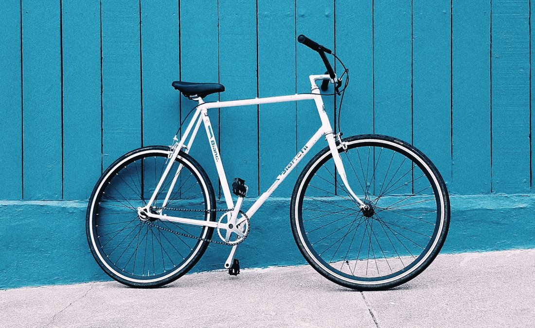 A photo of a white city racer bicycle leaned against a blue wall